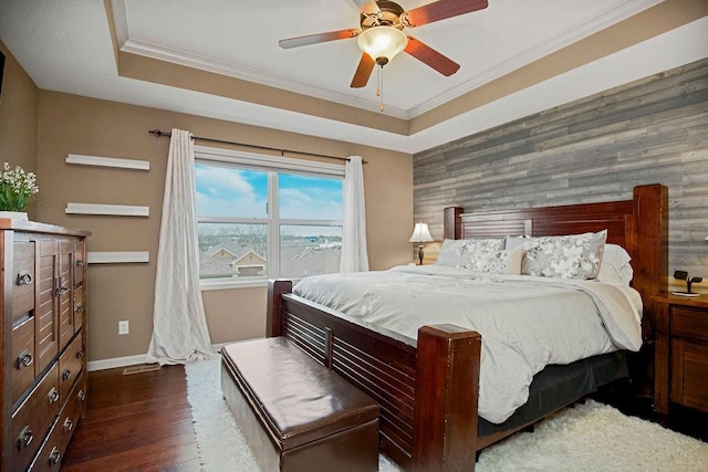 bedroom featuring ceiling fan, dark wood-type flooring, a raised ceiling, wooden walls, and ornamental molding