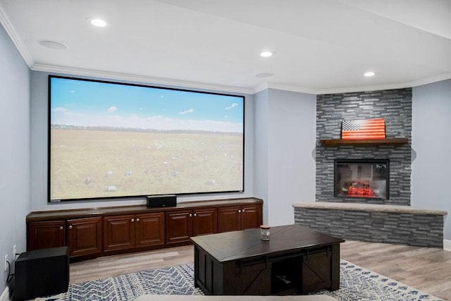 cinema featuring a stone fireplace, crown molding, and light hardwood / wood-style flooring