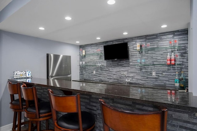 bar with dark stone countertops, stainless steel fridge, and sink