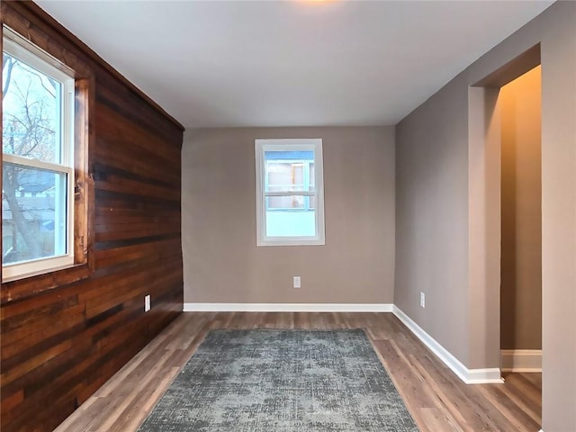 unfurnished room featuring plenty of natural light, dark hardwood / wood-style flooring, and wooden walls