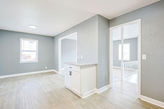 interior space with white cabinetry, light stone counters, and light wood-type flooring