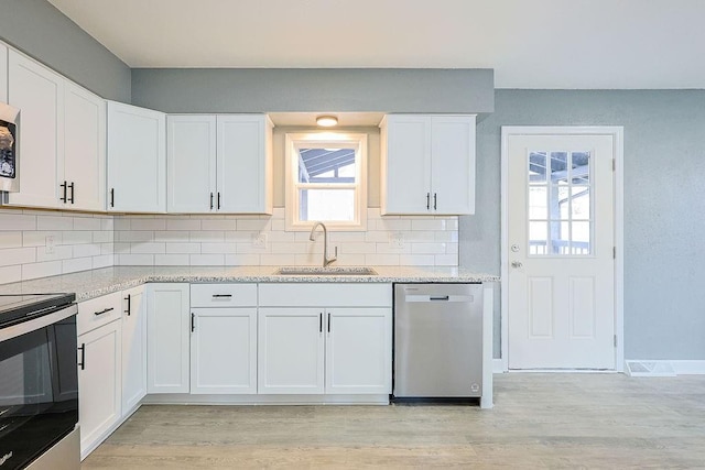 kitchen with decorative backsplash, range with electric cooktop, stainless steel dishwasher, sink, and white cabinets