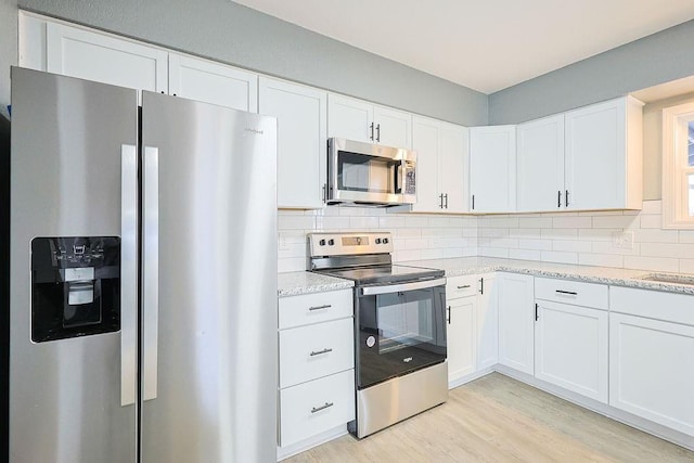 kitchen featuring white cabinetry, light stone counters, backsplash, light hardwood / wood-style floors, and appliances with stainless steel finishes