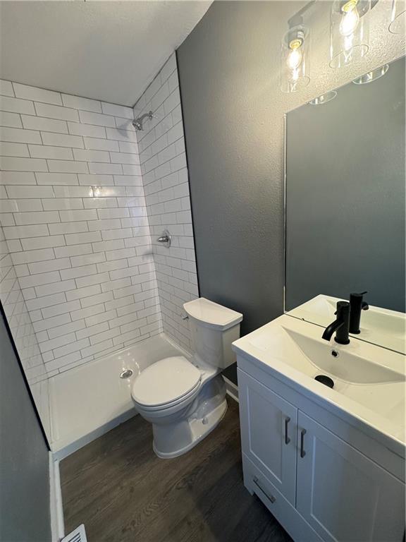 bathroom with hardwood / wood-style floors, vanity, toilet, and tiled shower