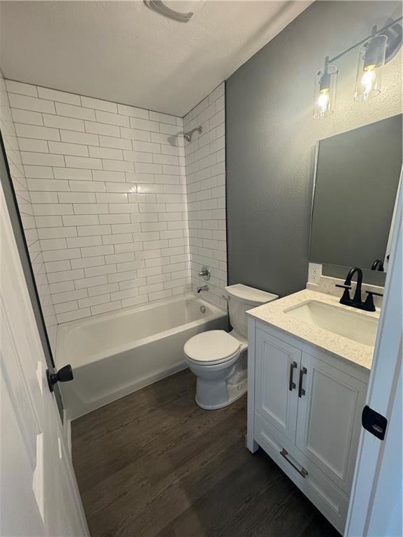 full bathroom with hardwood / wood-style floors, vanity, tiled shower / bath combo, and toilet