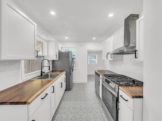 kitchen featuring wall chimney exhaust hood, stainless steel appliances, sink, white cabinetry, and butcher block counters