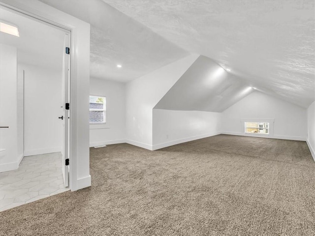 bonus room featuring a textured ceiling, light colored carpet, and lofted ceiling