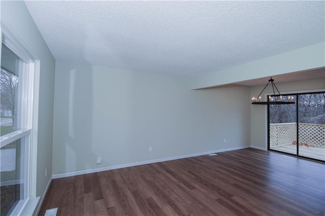 unfurnished room featuring dark hardwood / wood-style flooring, a textured ceiling, and a notable chandelier