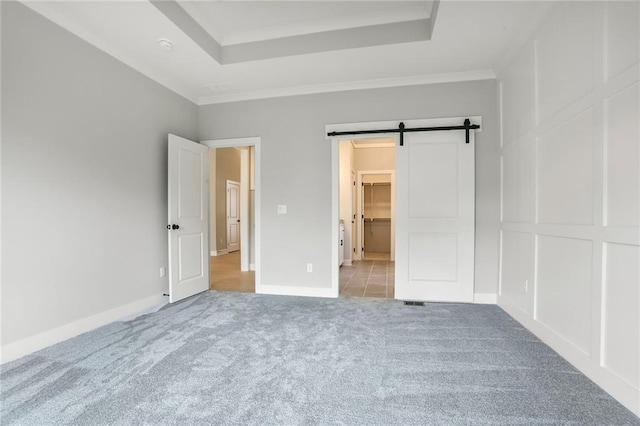 7050 NW Yulich Ct, Parkville, MO 64152 - unfurnished bedroom featuring carpet flooring, a barn door, a tray ceiling, a spacious closet, and crown molding