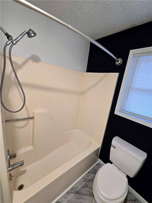 bathroom featuring a textured ceiling,  shower combination, and toilet