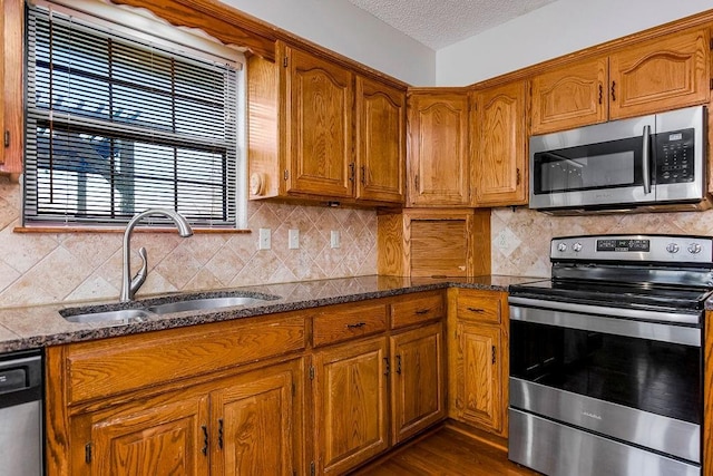 kitchen with sink, a textured ceiling, dark stone counters, stainless steel appliances, and backsplash