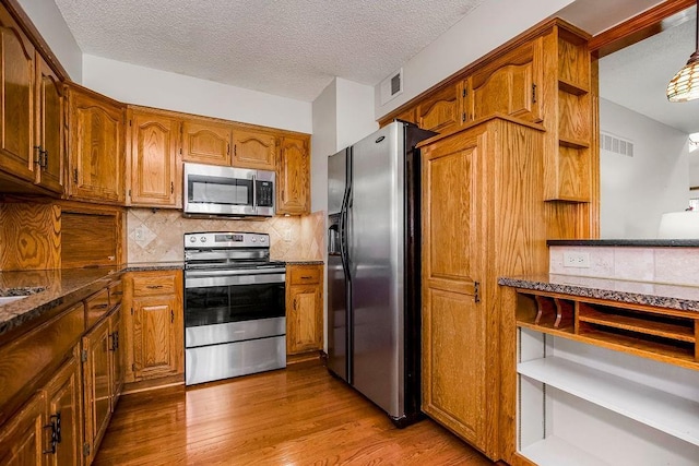 kitchen with tasteful backsplash, wood-type flooring, appliances with stainless steel finishes, and a textured ceiling