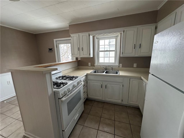 kitchen with white appliances, kitchen peninsula, tile patterned floors, white cabinets, and sink