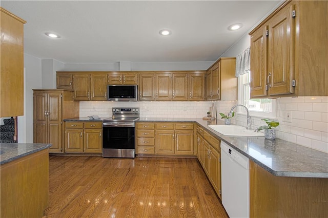 kitchen with appliances with stainless steel finishes, light hardwood / wood-style floors, dark stone counters, sink, and backsplash