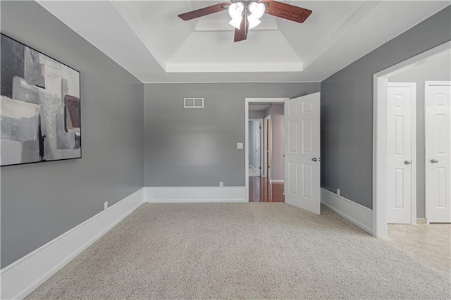 unfurnished bedroom with ceiling fan, a tray ceiling, and carpet flooring