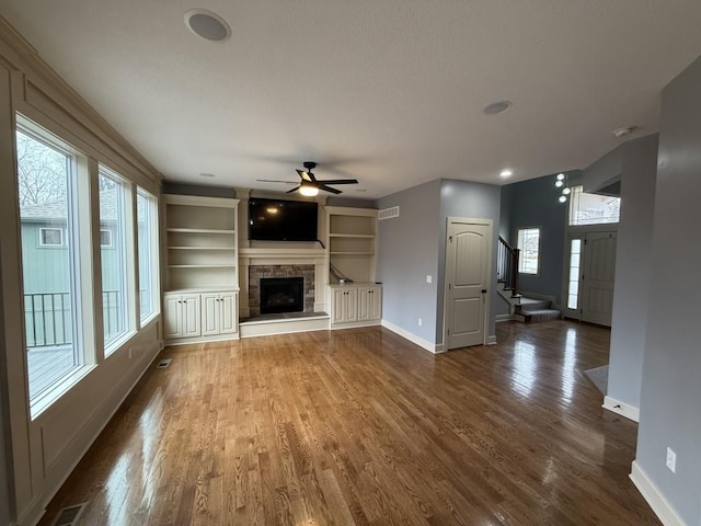 unfurnished living room with a fireplace, dark wood-type flooring, plenty of natural light, and built in shelves