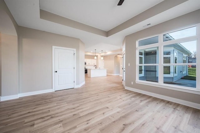 interior space with ceiling fan, a raised ceiling, and light hardwood / wood-style floors