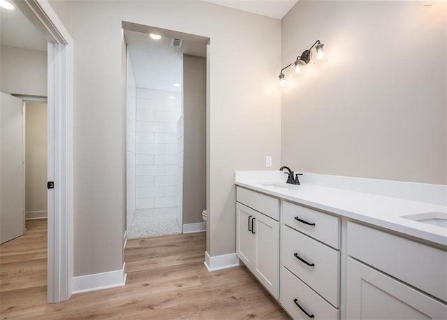 bathroom with toilet, vanity, a tile shower, and wood-type flooring