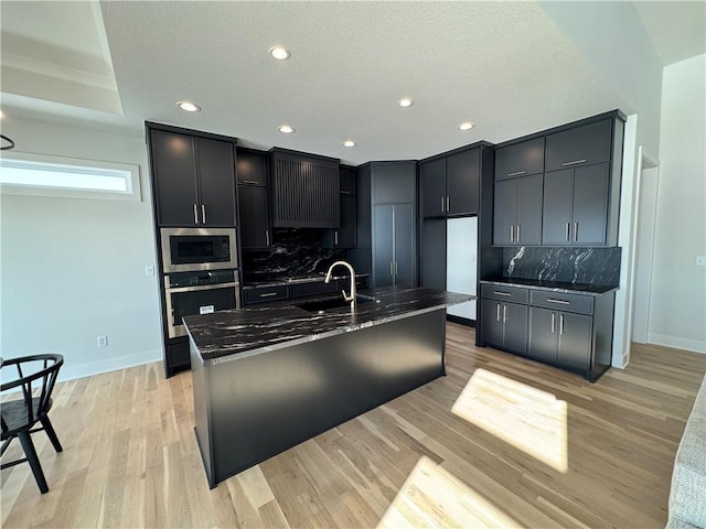 kitchen with stainless steel appliances, tasteful backsplash, light hardwood / wood-style floors, and dark stone counters