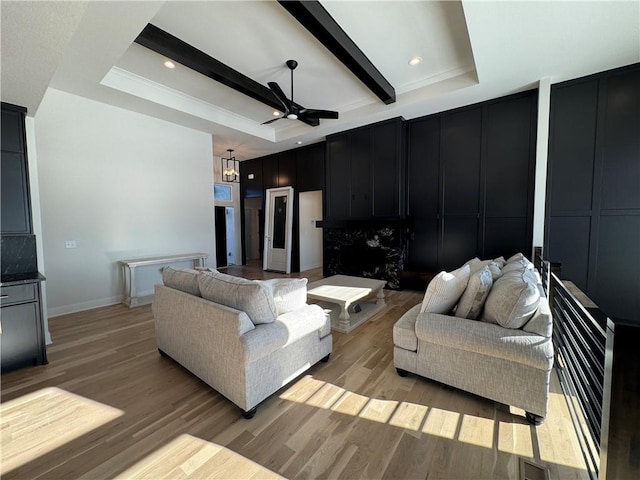 living room with a fireplace, beamed ceiling, light hardwood / wood-style flooring, ceiling fan with notable chandelier, and a tray ceiling