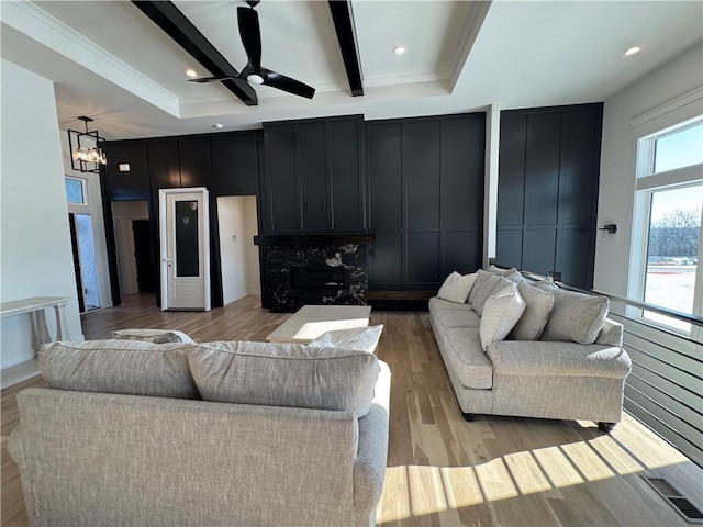 living room with ceiling fan with notable chandelier, beamed ceiling, and light hardwood / wood-style flooring