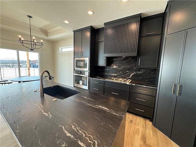 kitchen featuring extractor fan, stainless steel appliances, a raised ceiling, an island with sink, and sink