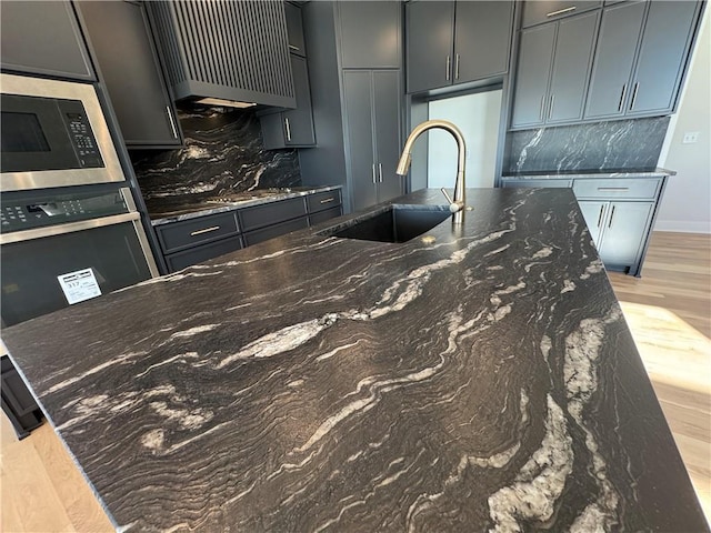 kitchen featuring sink, dark stone countertops, light hardwood / wood-style flooring, backsplash, and built in microwave