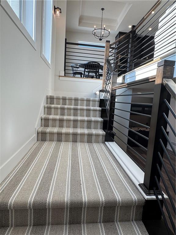 stairway featuring a healthy amount of sunlight, a raised ceiling, and a chandelier