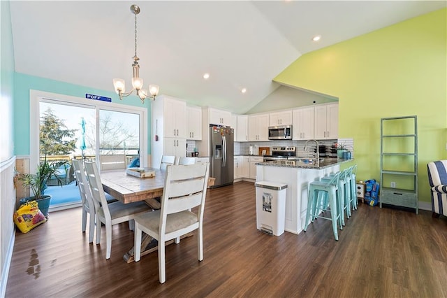 kitchen with hanging light fixtures, a kitchen breakfast bar, vaulted ceiling, white cabinets, and appliances with stainless steel finishes