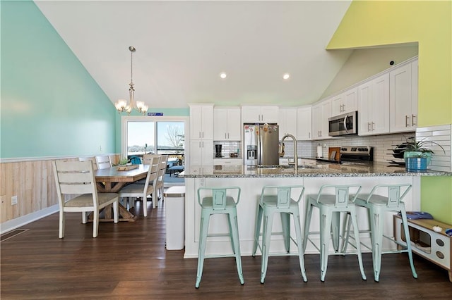 kitchen featuring stainless steel appliances, vaulted ceiling, decorative light fixtures, stone counters, and white cabinets