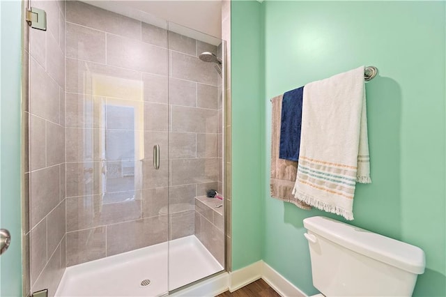 bathroom featuring toilet, a shower with door, and wood-type flooring