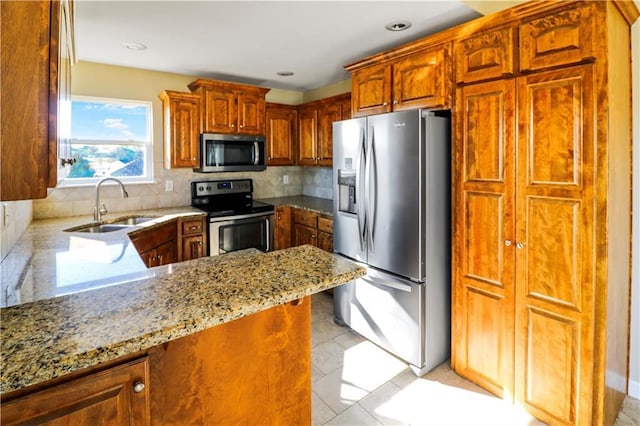 442 Redbud Ct, Warrensburg, MO 64093 - kitchen with appliances with stainless steel finishes, light stone counters, tasteful backsplash, a peninsula, and brown cabinets