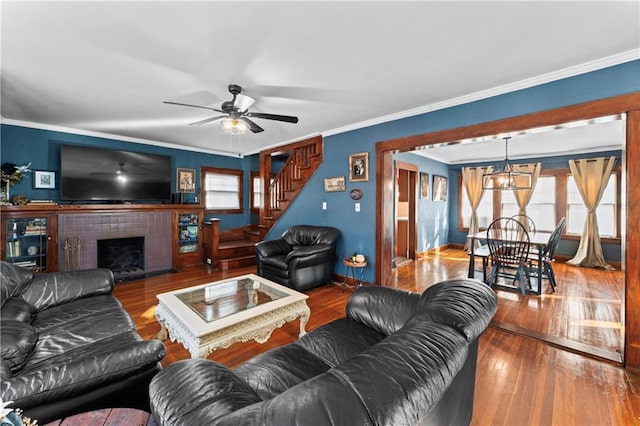 living room featuring hardwood / wood-style flooring, ornamental molding, ceiling fan with notable chandelier, and a tile fireplace