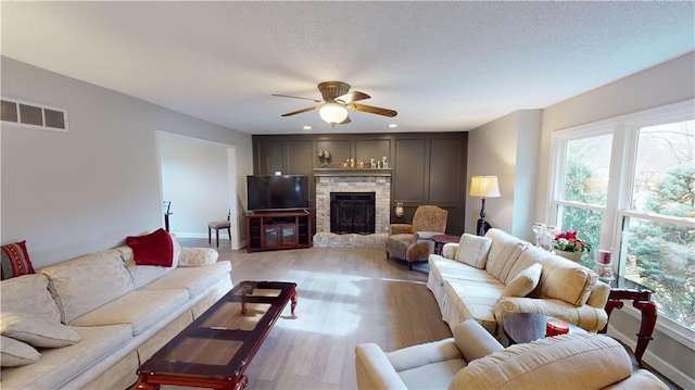 living room with ceiling fan, a wealth of natural light, light hardwood / wood-style floors, and a fireplace