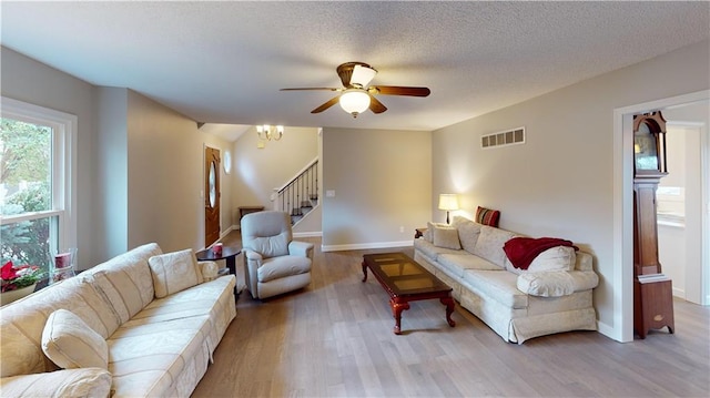 living room with ceiling fan with notable chandelier, a textured ceiling, and light hardwood / wood-style floors