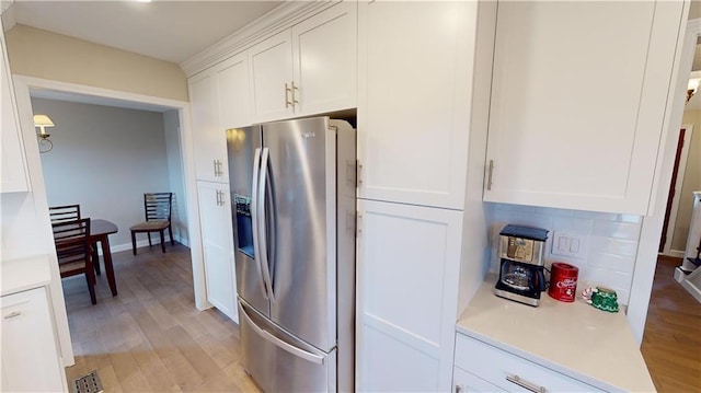 kitchen featuring tasteful backsplash, light wood-type flooring, stainless steel fridge with ice dispenser, and white cabinetry