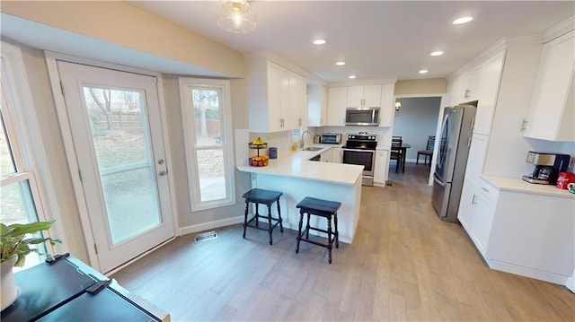 kitchen with kitchen peninsula, a breakfast bar area, stainless steel appliances, white cabinets, and sink