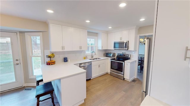 kitchen featuring a kitchen bar, stainless steel appliances, backsplash, light wood-type flooring, and white cabinets