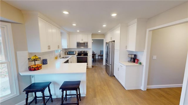 kitchen with a breakfast bar, sink, light wood-type flooring, stainless steel appliances, and white cabinets