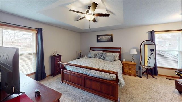 carpeted bedroom with ceiling fan, a raised ceiling, and multiple windows