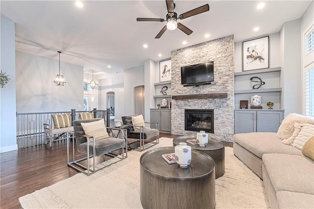 living room with a stone fireplace, wood-type flooring, built in features, and ceiling fan