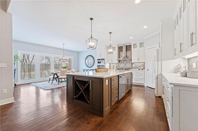 kitchen with appliances with stainless steel finishes, pendant lighting, an island with sink, white cabinets, and wall chimney range hood