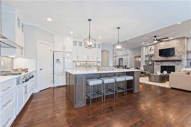 kitchen featuring a kitchen island with sink, hanging light fixtures, white fridge with ice dispenser, white cabinets, and a kitchen bar