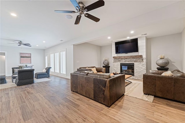 living room featuring ceiling fan, a fireplace, and light wood-type flooring