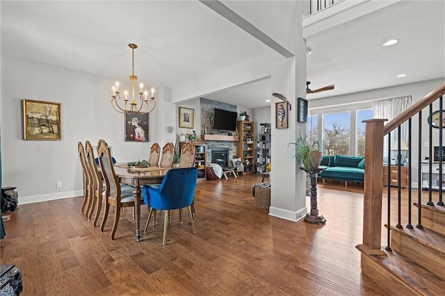 dining room with dark wood-type flooring, a fireplace, and ceiling fan with notable chandelier