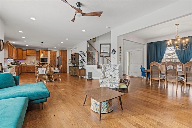 living room with ceiling fan with notable chandelier and light hardwood / wood-style flooring