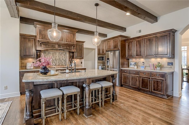 kitchen with pendant lighting, light stone counters, light hardwood / wood-style floors, stainless steel appliances, and a center island with sink