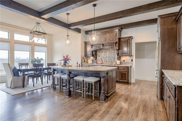 kitchen featuring hardwood / wood-style floors, decorative light fixtures, light stone countertops, and a center island with sink