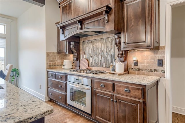 kitchen with premium range hood, light stone counters, dark brown cabinets, appliances with stainless steel finishes, and decorative backsplash