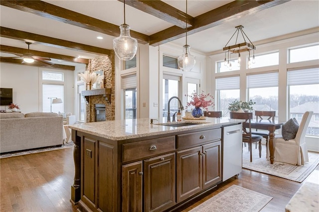 kitchen featuring sink, light stone counters, dishwasher, pendant lighting, and a kitchen island with sink